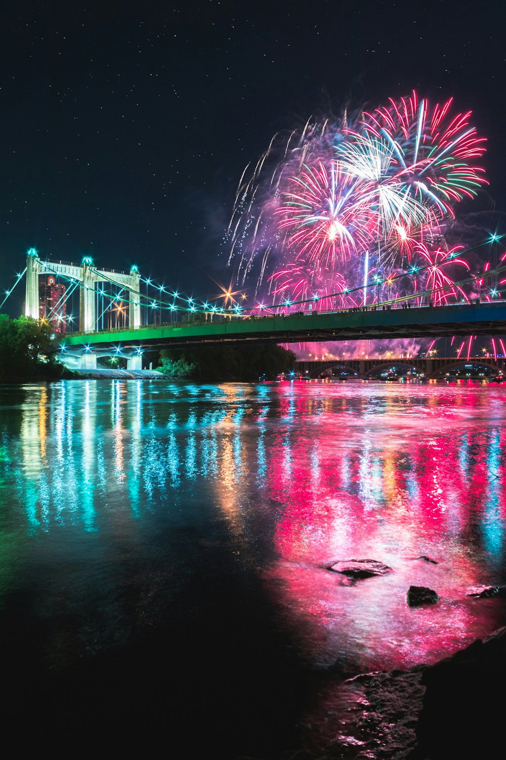 fireworks display over bridge over river during nighttime