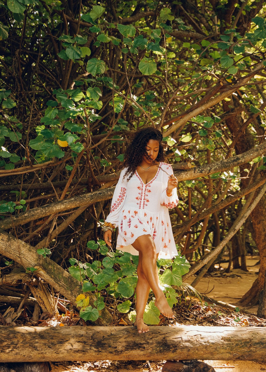 woman in white and red floral dress standing on brown tree trunk during daytime