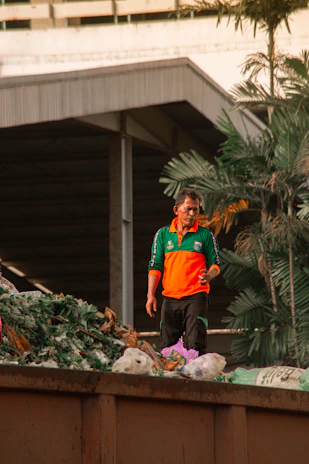 A team member in a DinoHaul shirt helping a customer load debris into a dumpster with palm trees in the background.