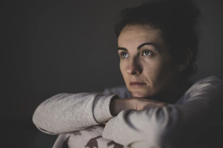 A woman with dark hair resting her chin on her hands in dim light