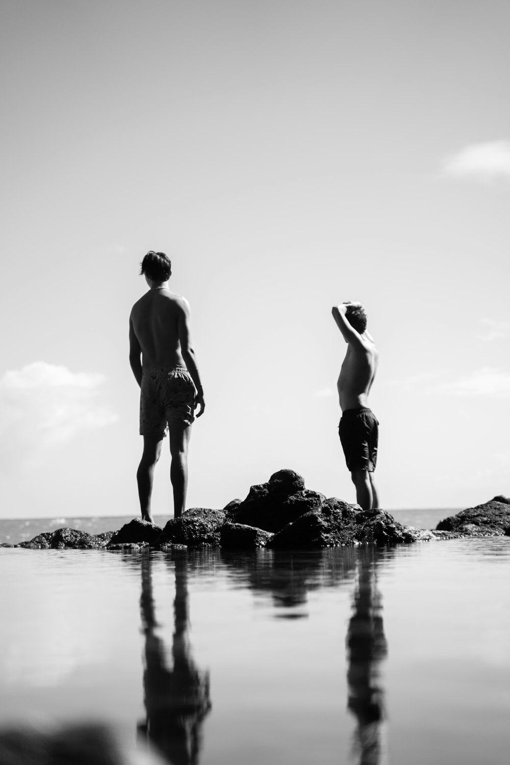 2 men standing on rock in grayscale photography