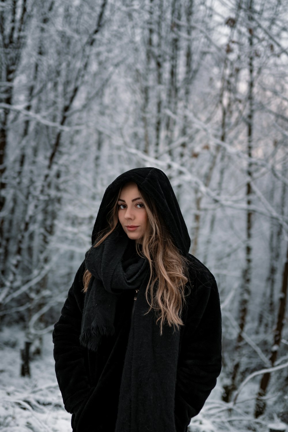 woman in black hoodie standing near snow covered trees during daytime