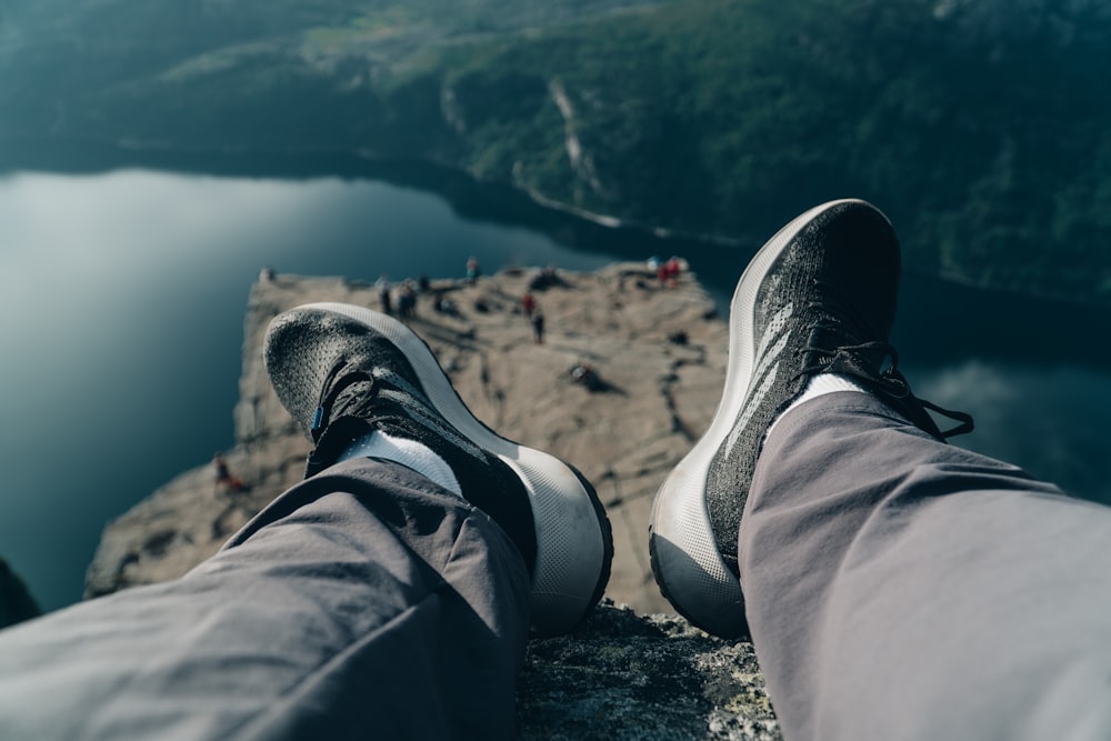 person in black pants and gray sneakers sitting on rock