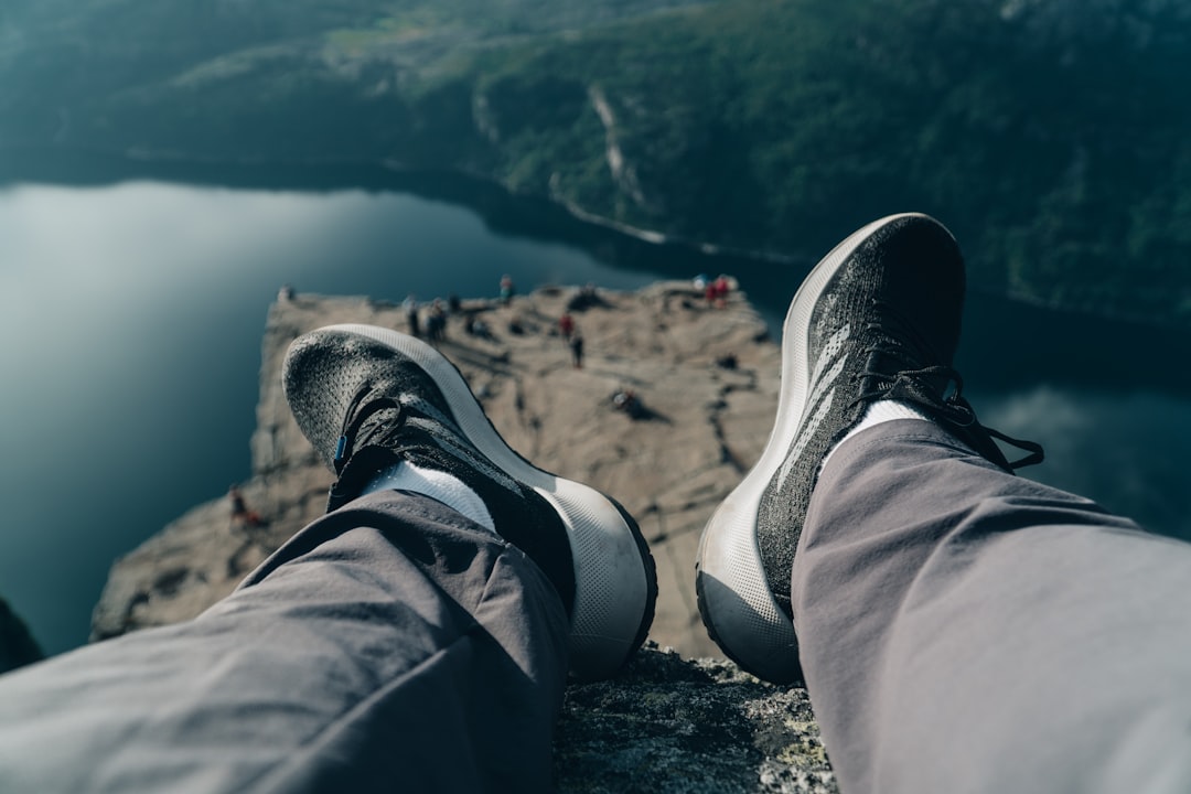 person in black pants and gray sneakers sitting on rock