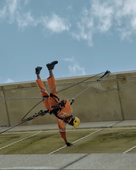 Technician in pistachio green gear installing safety lifeline on a tall building facade under clear sky.