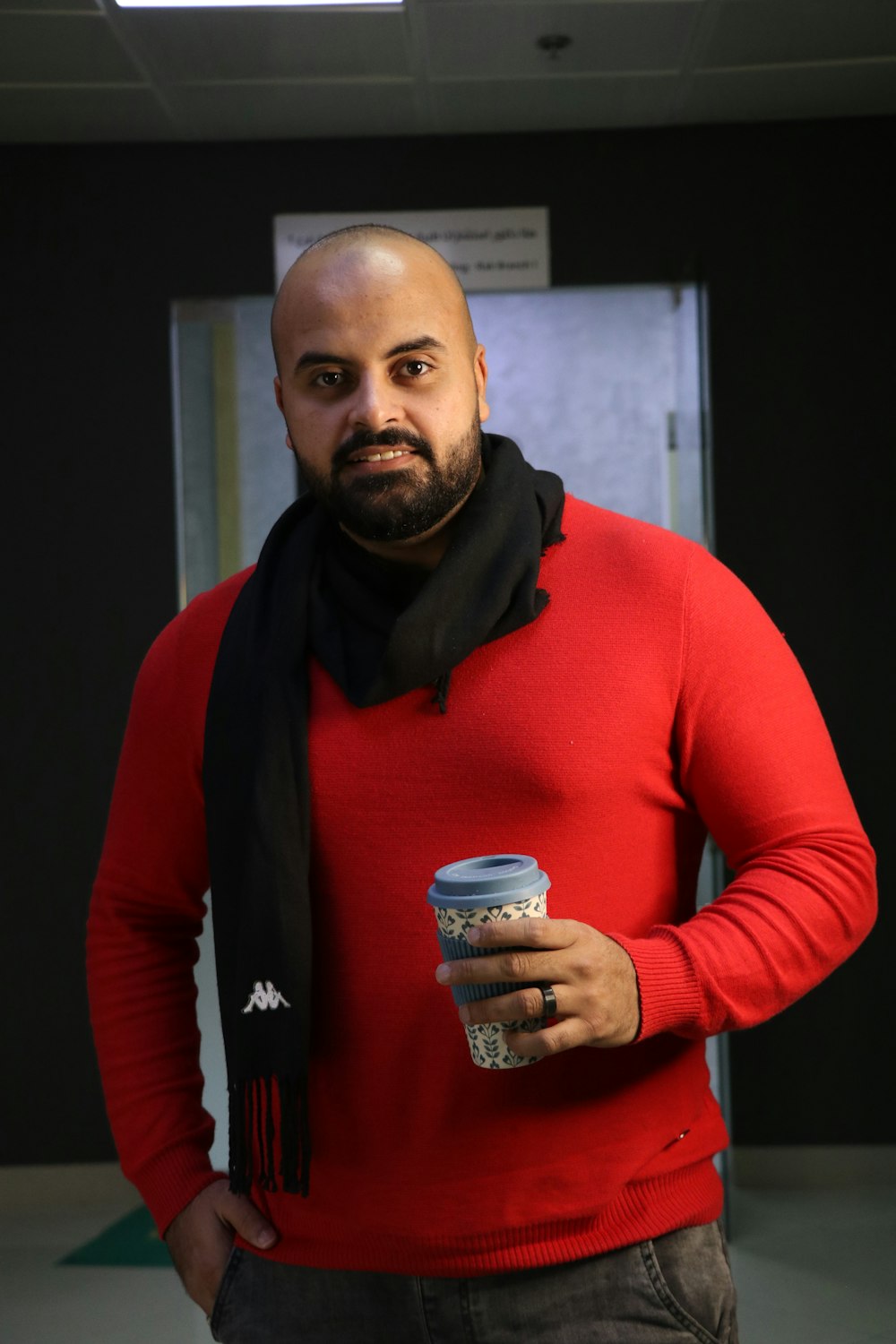 man in red sweater holding white and blue ceramic mug