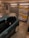 A garage interior featuring a car parked inside. The walls are decorated with a variety of international license plates. A shelf full of tools and car maintenance items is visible on the side. A poster of a well-known fictional character is also on display.
