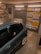 A garage interior featuring a car parked inside. The walls are decorated with a variety of international license plates. A shelf full of tools and car maintenance items is visible on the side. A poster of a well-known fictional character is also on display.