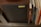 A speaker with a label reading 'Harbeth' is positioned next to a row of books or vinyl records. The wooden finish of the speaker and dark-colored fabric cover can be seen, alongside the spines of various books or records in assorted colors and styles.