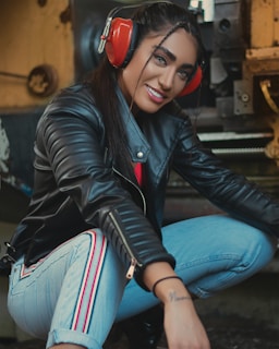 woman in black leather jacket and blue denim jeans wearing red and black headphones