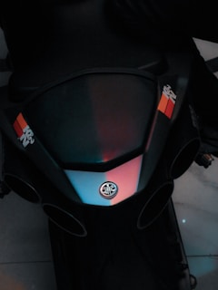 A close-up view of a motorcycle's front section featuring a sleek design with a prominent logo in the center. Two colorful sticker stripes add contrast to the dark body of the bike.
