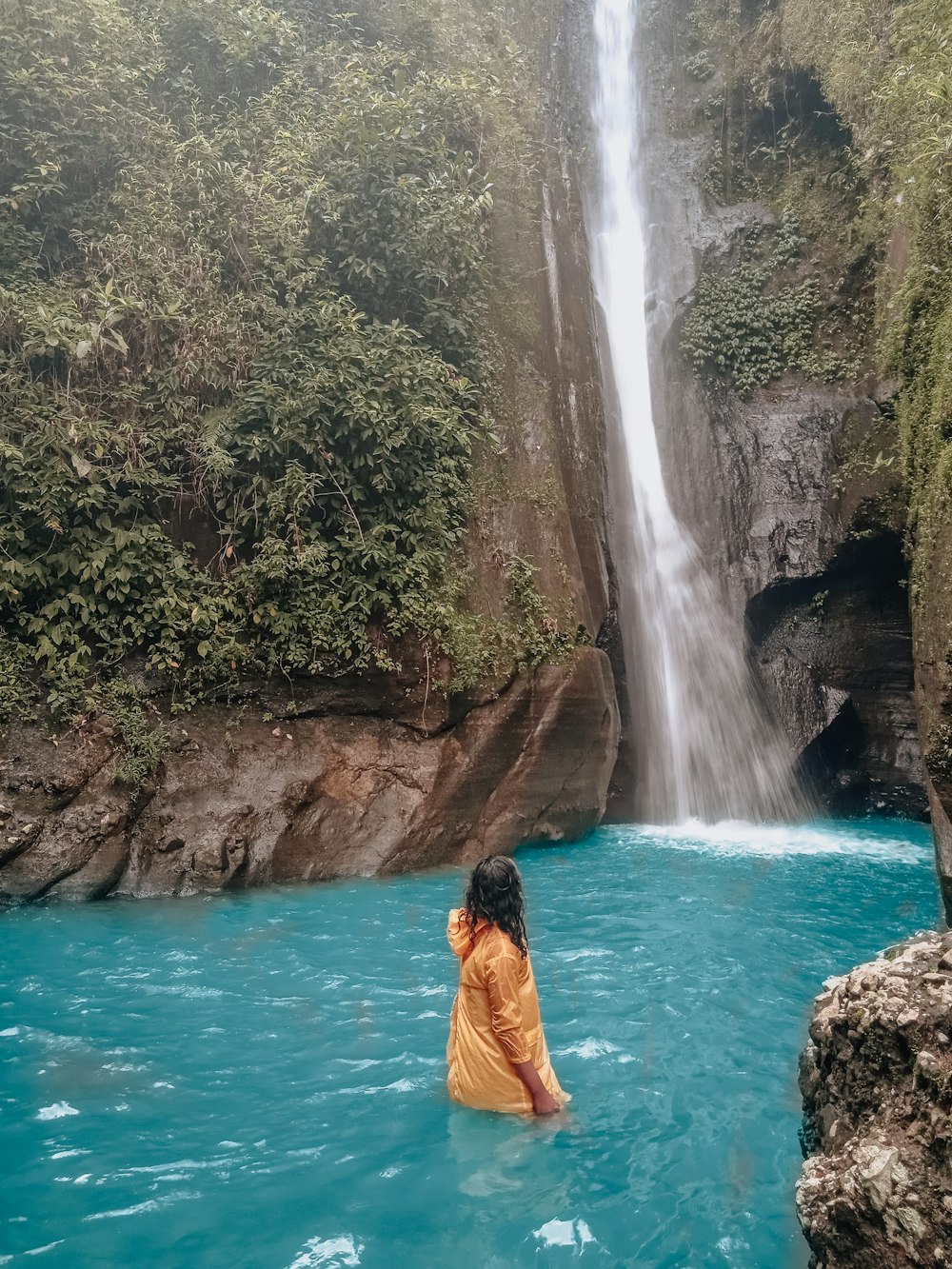 woman in orange dress sitting on rock near waterfalls during daytime