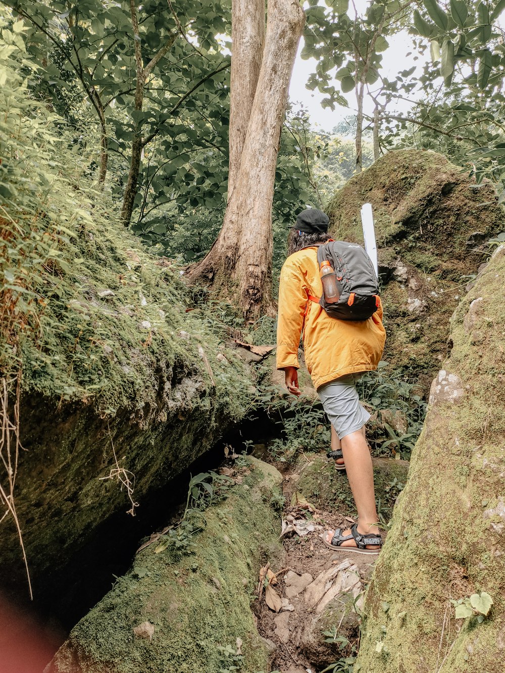 man in orange jacket climbing on brown rock