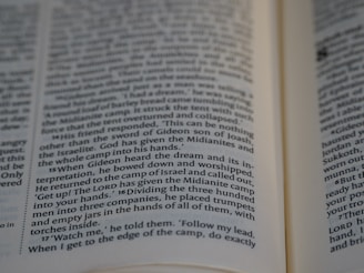 A close-up image of an open book showing text from what appears to be a religious or biblical passage. The text is focused and legible, with lines in small, printed font.