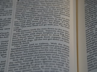 Close-up view of an open book showing text from a religious or historical scripture. The passage focuses on an instruction involving the behavior of men drinking water, emphasizing the separation based on how they drink.
