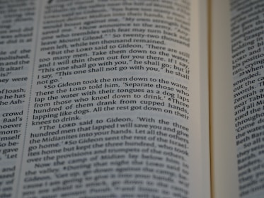 Close-up view of an open book showing text from a religious or historical scripture. The passage focuses on an instruction involving the behavior of men drinking water, emphasizing the separation based on how they drink.