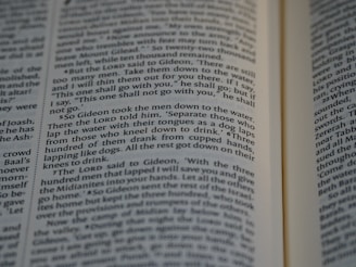 Close-up view of an open book showing text from a religious or historical scripture. The passage focuses on an instruction involving the behavior of men drinking water, emphasizing the separation based on how they drink.