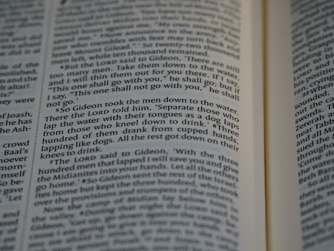 Close-up view of an open book showing text from a religious or historical scripture. The passage focuses on an instruction involving the behavior of men drinking water, emphasizing the separation based on how they drink.