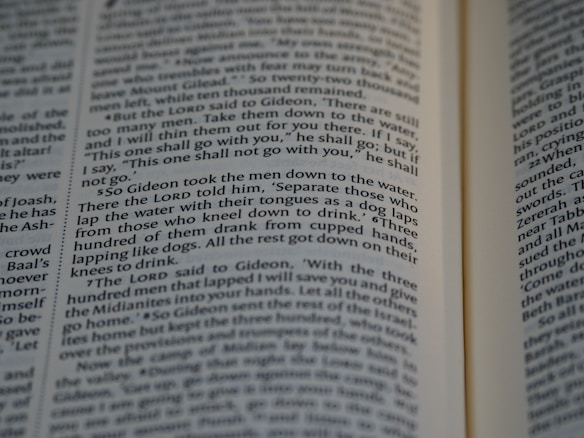 Close-up view of an open book showing text from a religious or historical scripture. The passage focuses on an instruction involving the behavior of men drinking water, emphasizing the separation based on how they drink.