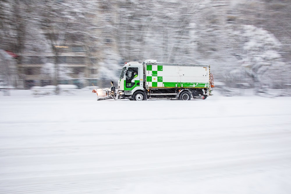 日中の雪に覆われた道路を走る緑色のトラック