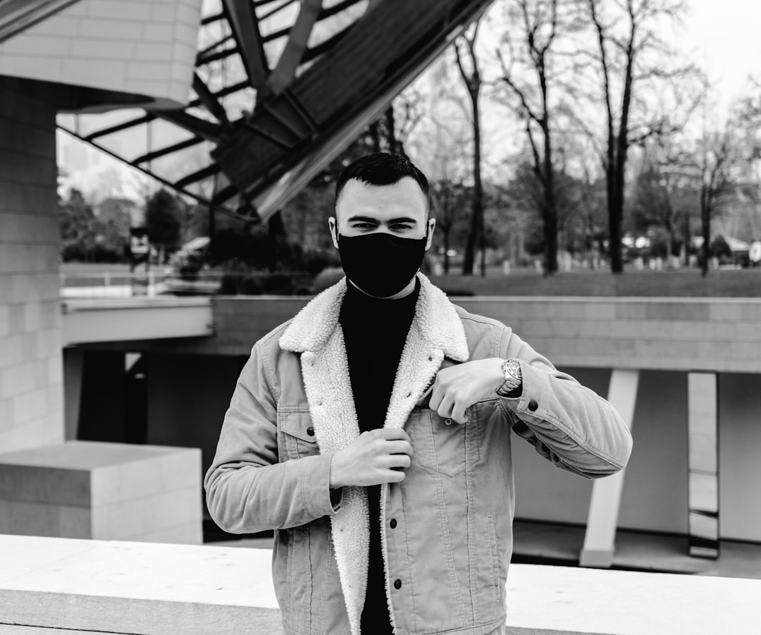 grayscale photo of man wearing coat and mask