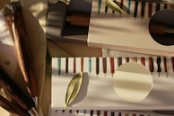 A collection of exquisitely crafted wooden pens displayed in elegant packaging, with a leaf delicately placed on top. The pens have a variety of colorful and glossy patterns, each with a distinct appearance. The soft, warm lighting creates gentle shadows, adding depth and character to the scene.