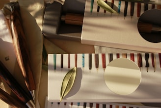A collection of exquisitely crafted wooden pens displayed in elegant packaging, with a leaf delicately placed on top. The pens have a variety of colorful and glossy patterns, each with a distinct appearance. The soft, warm lighting creates gentle shadows, adding depth and character to the scene.