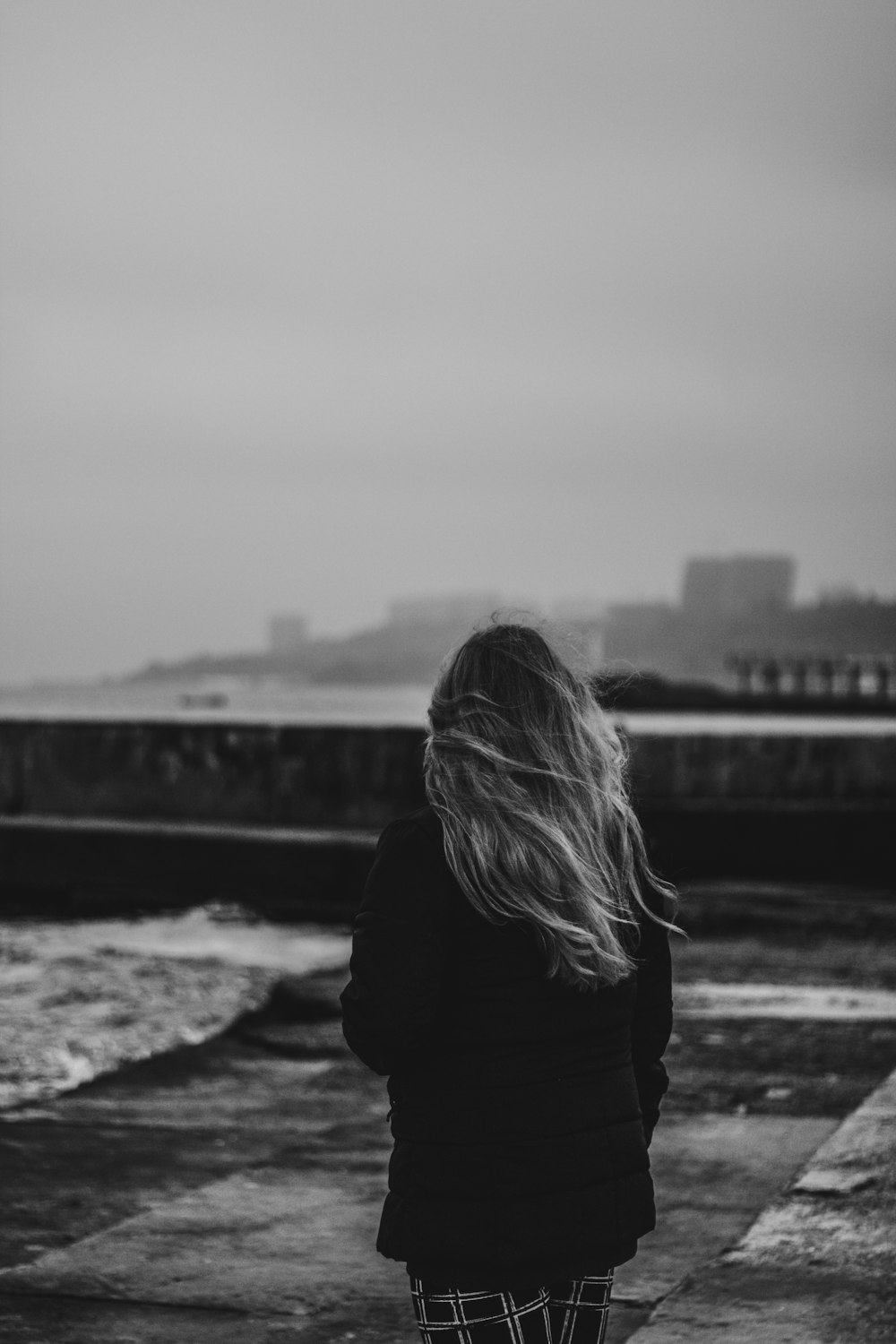 grayscale photo of woman in black jacket standing on rock