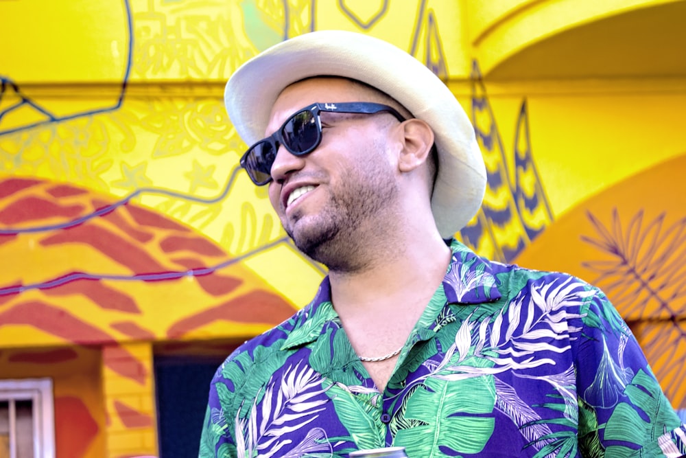 man in green and blue floral button up shirt wearing black sunglasses and beige hat