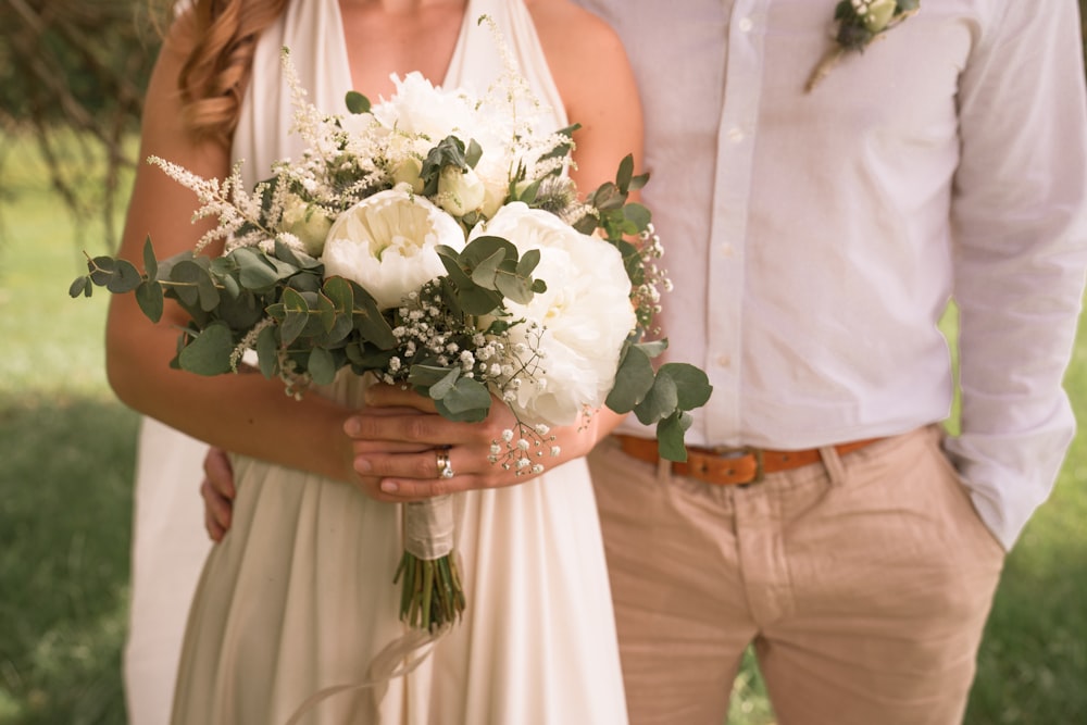Femme en robe blanche sans manches tenant un bouquet de fleurs blanches