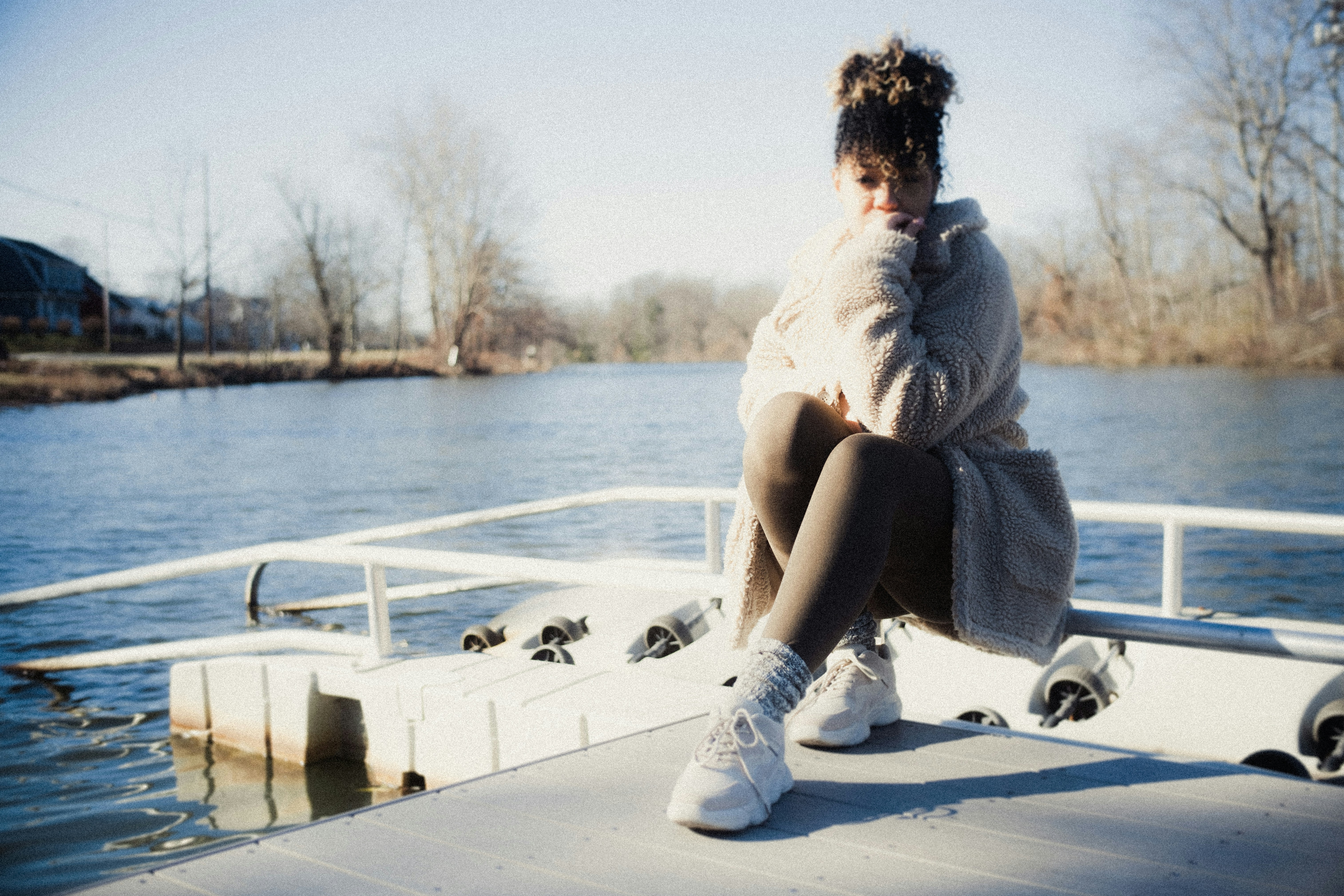 woman in white sweater and gray pants sitting on white wooden dock during daytime