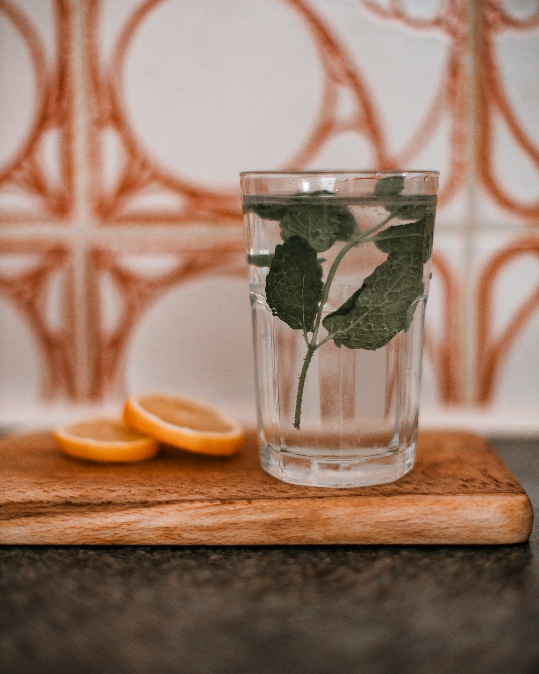 clear drinking glass with water and sliced lemon on brown wooden chopping board