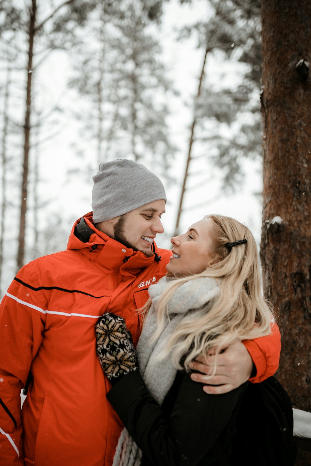 woman in red jacket and gray knit cap standing beside brown tree during daytime