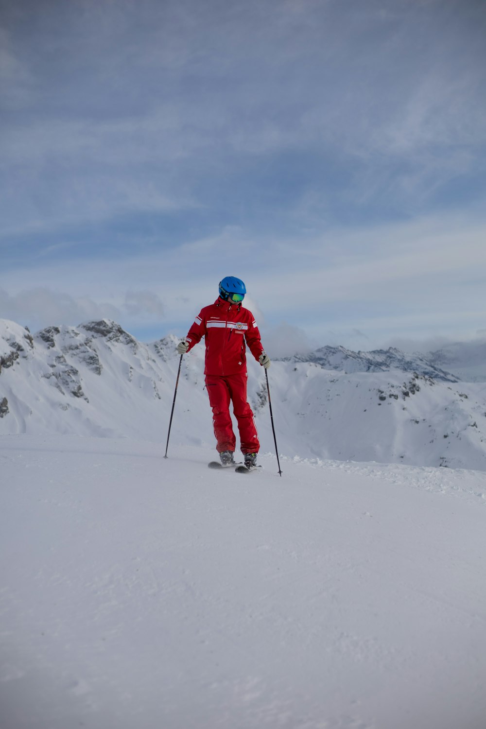 Persona con chaqueta roja y pantalones negros montando hojas de esquí en la montaña cubierta de nieve durante el día