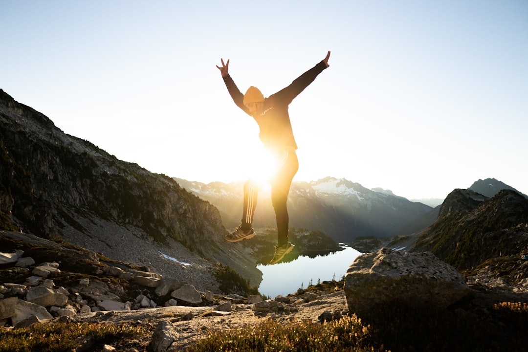 woman in white long sleeve shirt and black pants jumping on rocky mountain during daytime