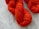 Bundles of bright orange yarn are placed against a textured white wooden surface. The yarn is neatly coiled, exhibiting a thick and uniform texture.