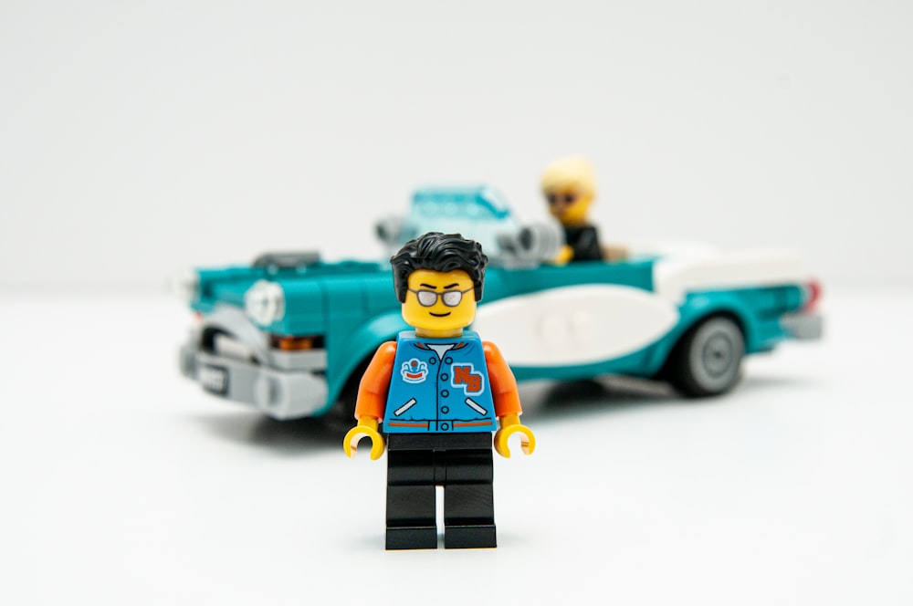 Mini figura de Lego junto al coche de juguete azul y amarillo