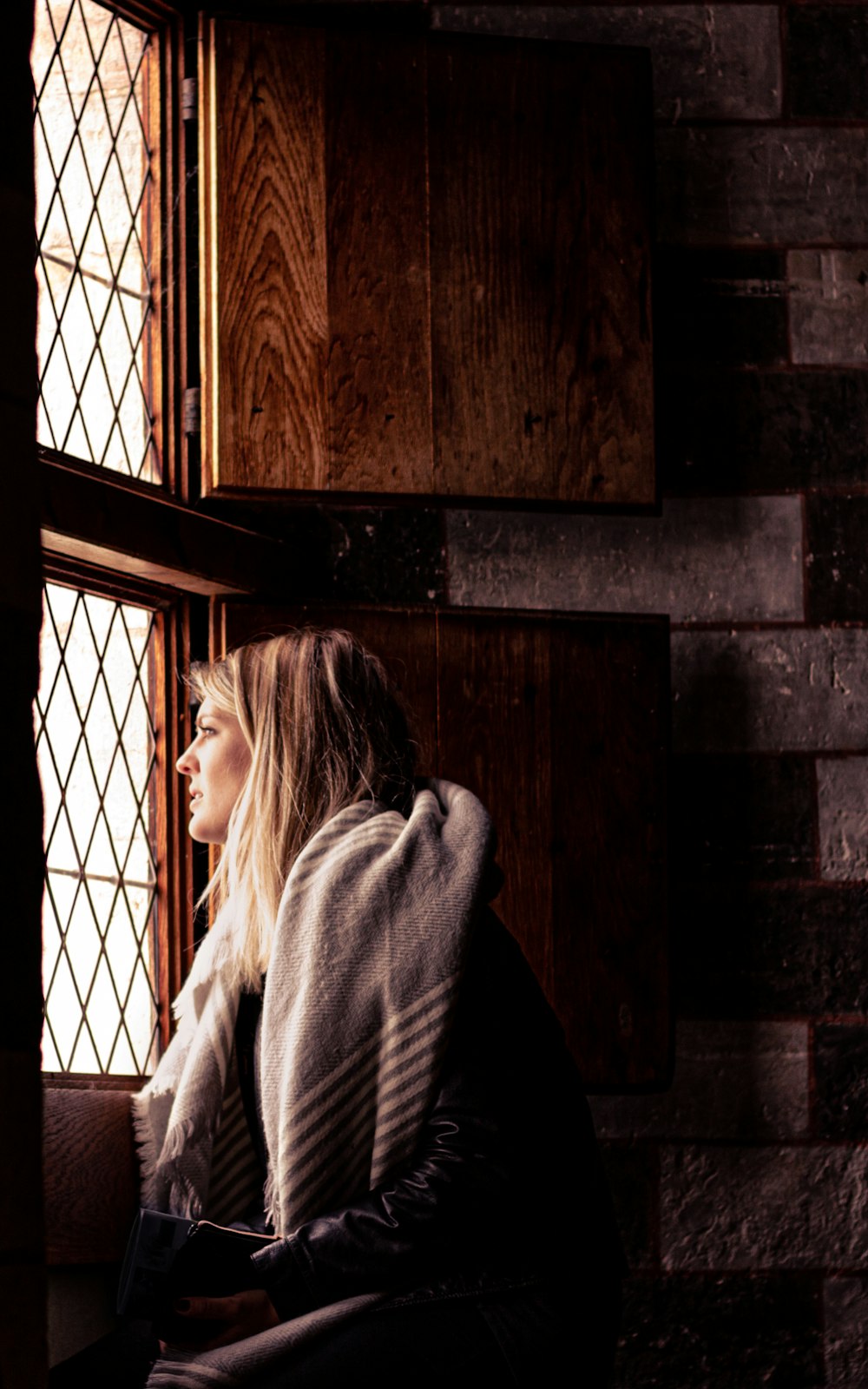 woman in gray sweater standing beside brown wooden wall