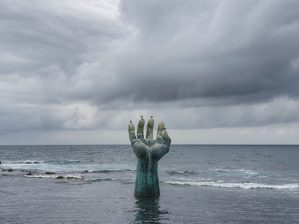 person raising hand on sea under cloudy sky during daytime