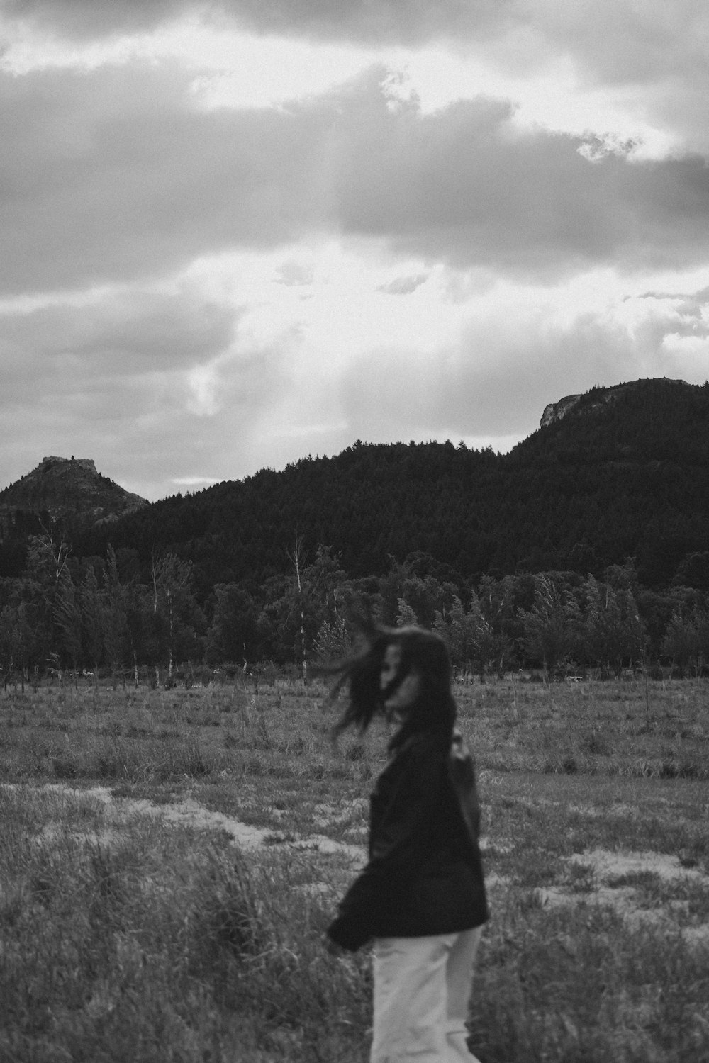 grayscale photo of woman in black jacket standing on grass field