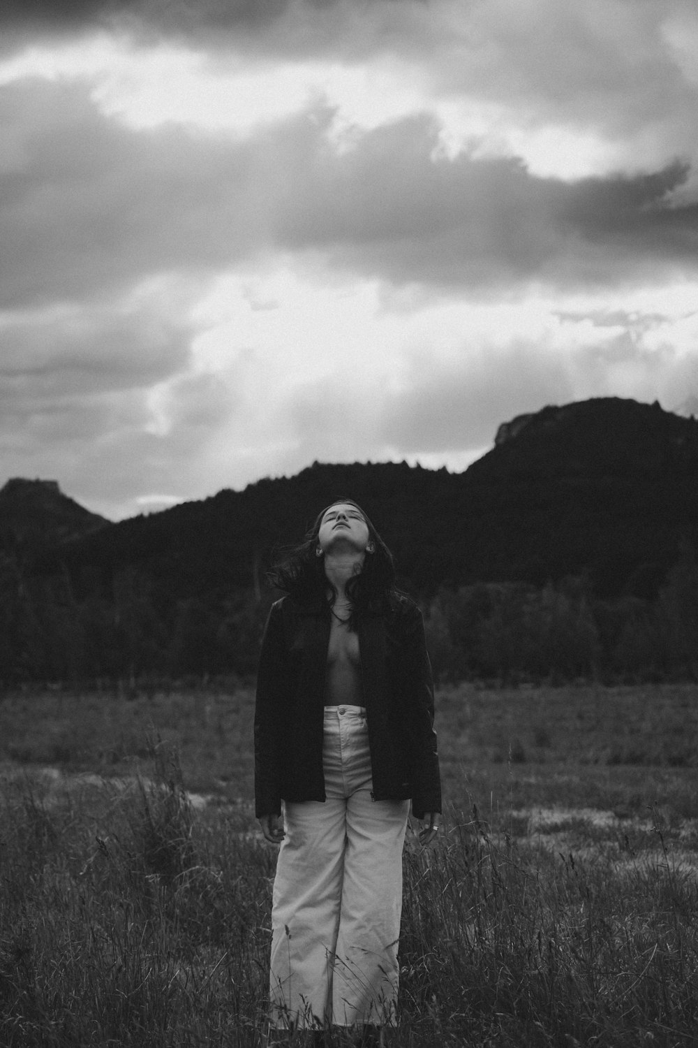 grayscale photo of woman in black jacket and white pants standing on grass field