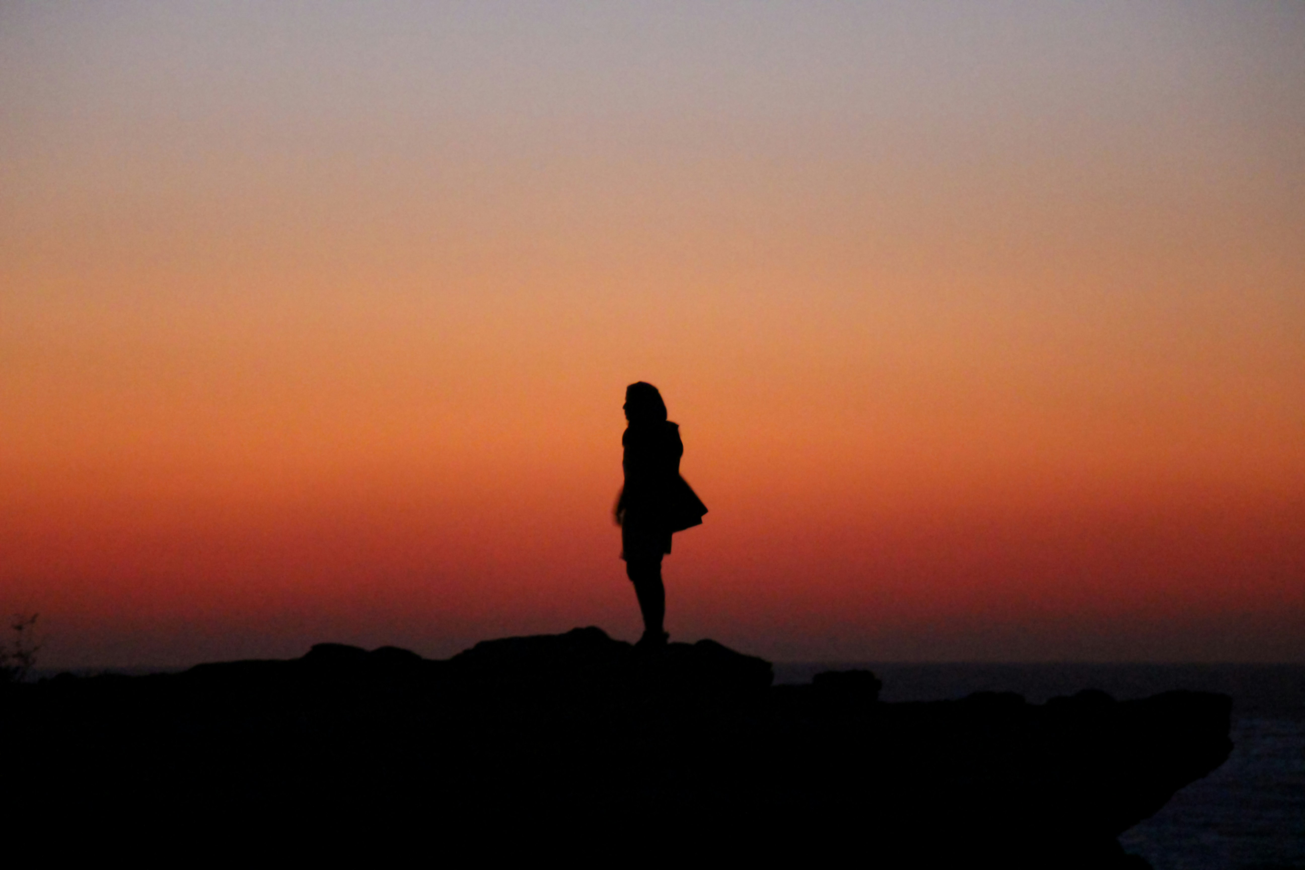silhouette of person standing on rock during sunset
