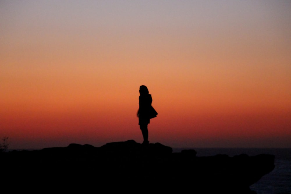 silhouette of person standing on rock during sunset