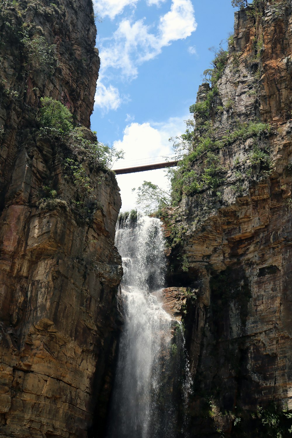 waterfalls between brown rocky mountain under blue sky during daytime