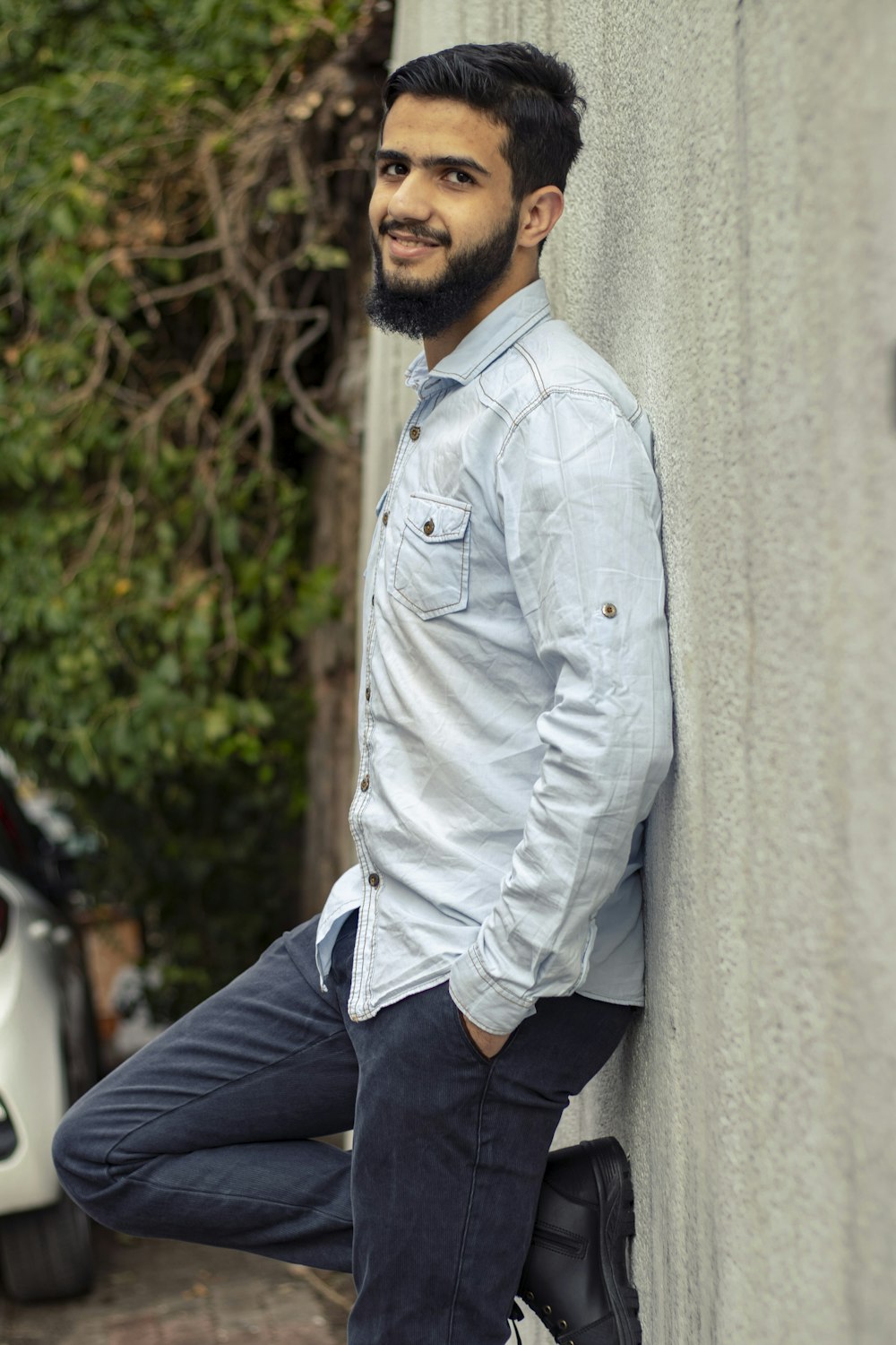 Hombre con camisa de vestir blanca y jeans vaqueros azules sentado en una pared de concreto durante el día