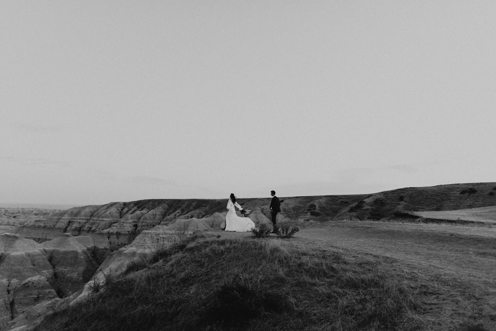 couple sitting on rock formation in grayscale photography