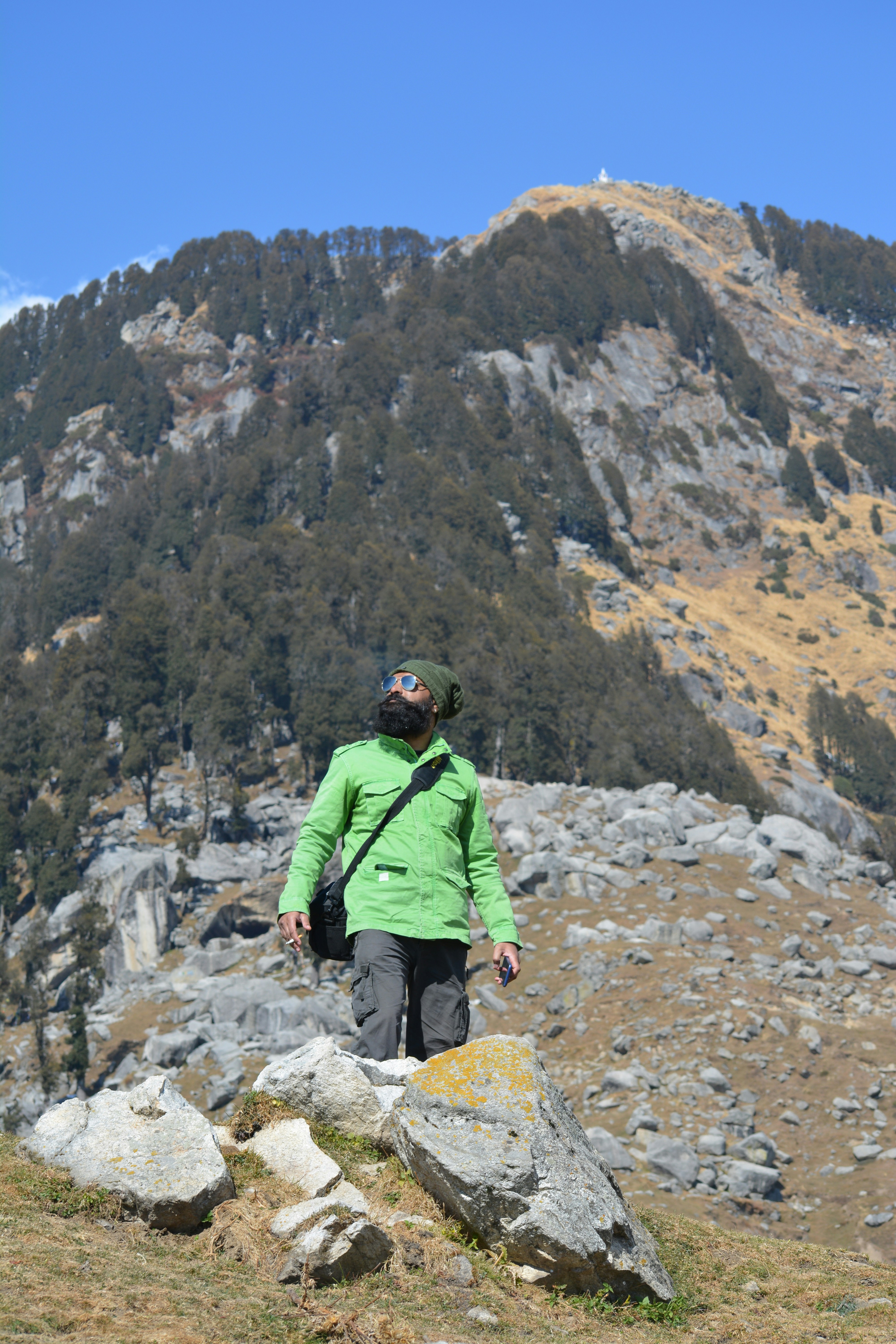 Uomo in giacca verde e pantaloni marroni seduti sulla montagna di roccia durante il giorno