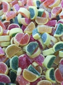 A colorful assortment of sugar-coated gummy candies shaped like citrus fruit slices in various shades of red, orange, yellow, and green.