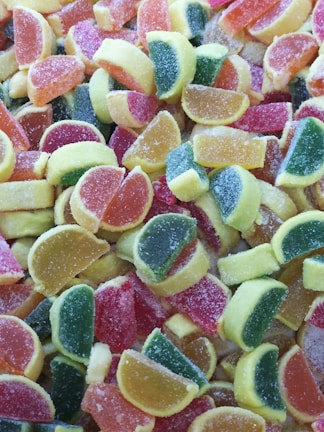 A colorful assortment of sugar-coated gummy candies shaped like citrus fruit slices in various shades of red, orange, yellow, and green.