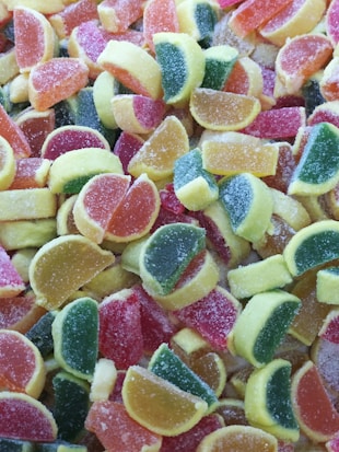 A colorful assortment of sugar-coated gummy candies shaped like citrus fruit slices in various shades of red, orange, yellow, and green.
